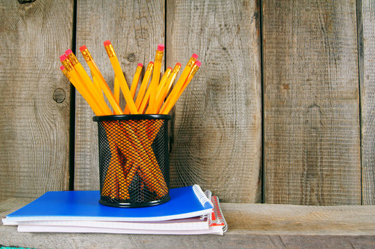 Pencils and writing-books on a wooden shelf.