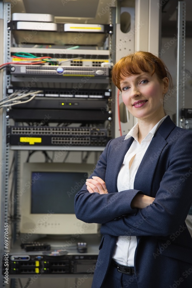 Poster Pretty computer technician smiling at camera beside server
