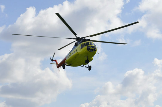 The yellow MI-8 helicopter flies against clouds.