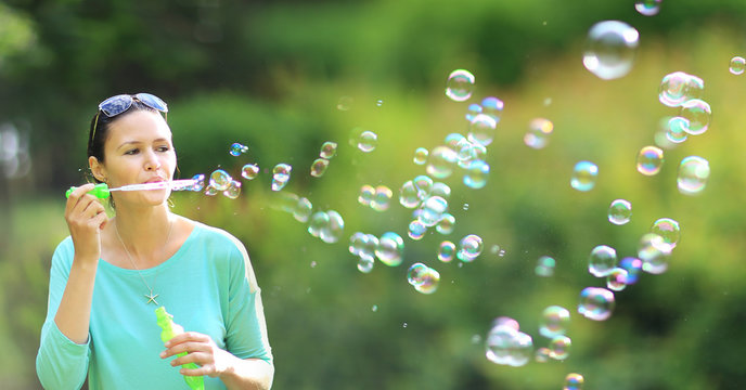 brunette girl blowing soap bubbles in sunlit park.