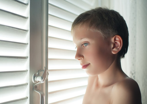 Funny Boy By Window With Blinds. Candid Portait. 