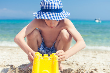 Funny child with panama playing on beach building castle