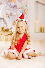 Beautiful little Santa girl near the Christmas tree.  Happy girl