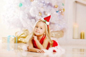 Beauty little Santa girl near the Christmas tree.  Happy girl wi