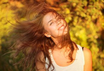 Fototapeta premium Beautiful smiling woman in a field at sunset with flying hair