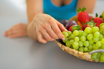 Closeup on young woman with fruits plate eating grape