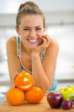Portrait of happy young woman with halloween orange in kitchen