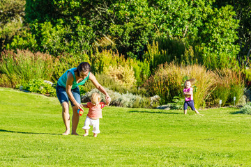 Mädchen macht erste Schritte im Park an den Händen ihrer Mutter