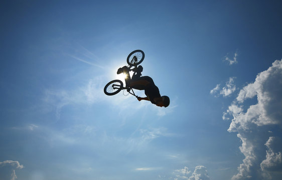 a BMX rider performing an air trick back-flip against blue sky