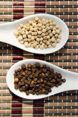black and white peppercorns on white spoons