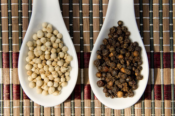 black and white peppercorns on white spoons