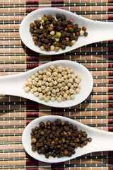 black white and color peppercorns on white spoons