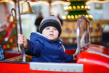 Adorable little boy on a carousel at Christmas funfair or market