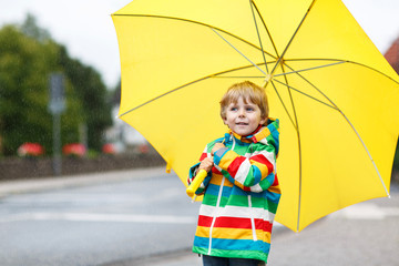 Adorable toddler boy with yellow umbrella and colorful jacket ou