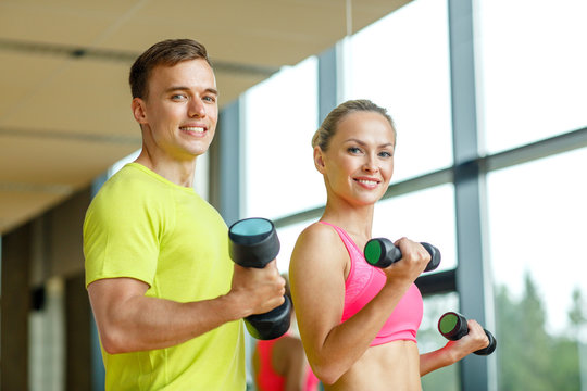 smiling man and woman with dumbbells in gym