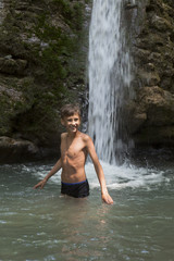 Счастливый мальчик купается в холодной воде водопада