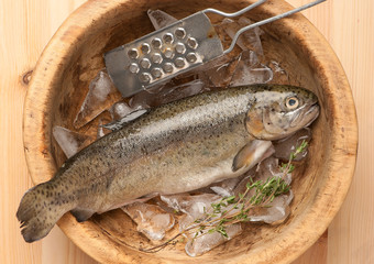 Raw trout fish with ice in wooden bowl