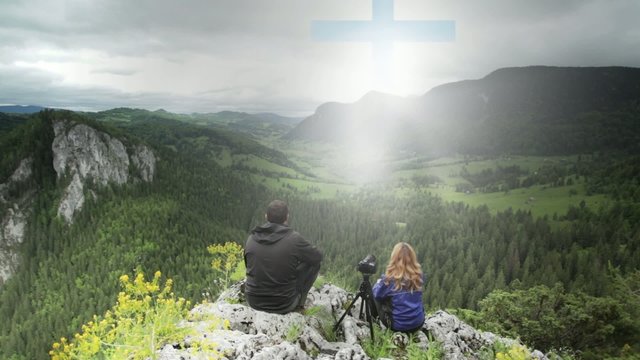 Man and woman on top of the mountain looking at a cross