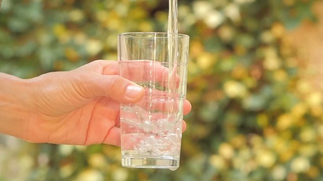 close up of hand holding glass filling with water slow motion