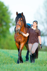 Young girl walking with a horse in the field