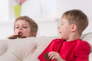 Portrait of two kids eating in white sofa.