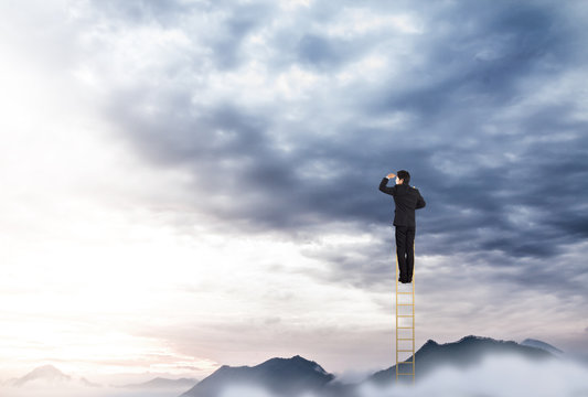 Businessman climbing on a ladder over mountain looking ahead