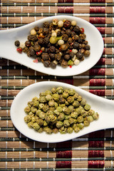 green and color peppercorns on white spoons