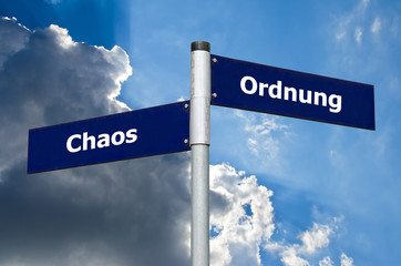 Straßenschild vor bewölktem/blauem Himmel welches die Wahl zwischen Chaos und Ordnung symbolisiert