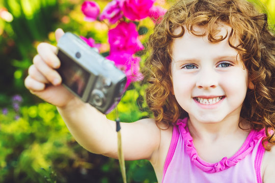 Happy little girl taking self photo on a summer garden.