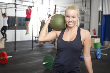 Smiling blonde woman with slam ball at fitness gym