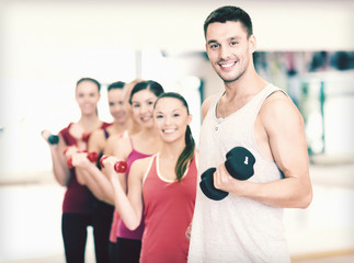 group of smiling people with dumbbells in the gym