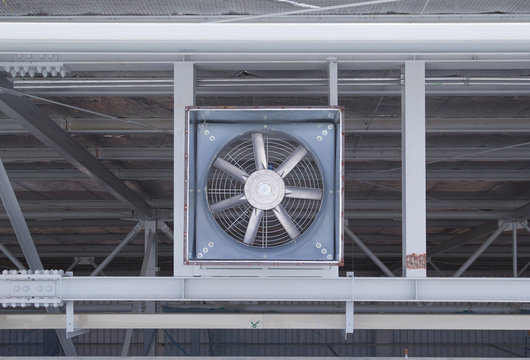 Industrial wall exhaust fan mounted overhead metal ceiling beam structure featuring steel blades, airflow ventilation system, warehouse cooling equipment, clean technical engineering.