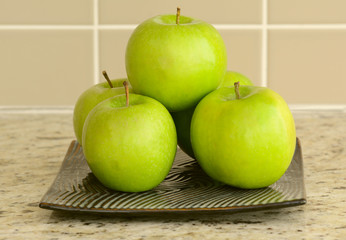 Fresh green apples in flat square plate on kitchen counter top
