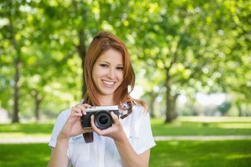 Pretty redhead holding her camera in the park