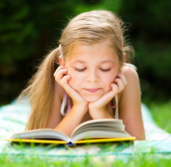Little girl is reading a book outdoors