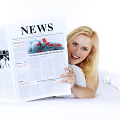 Woman is reading newspaper in bed