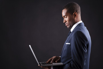 Young business man with a laptop over dark background