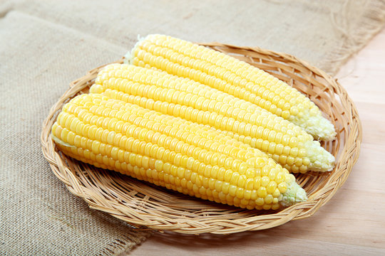 Corn on the cob in a basket on a wooden table.