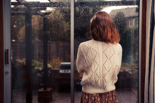 Young woman by window looking at the rain