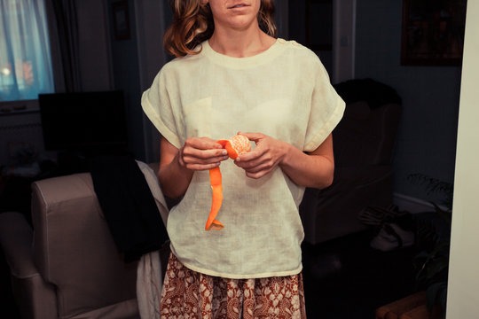 Young woman peeling orange at home