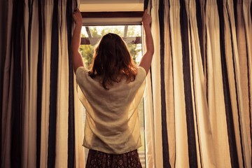 Fototapeta na wymiar Young woman opening the curtains at sunrise