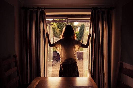 Young woman opening the curtains at sunrise