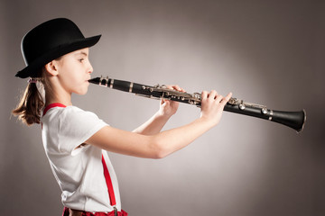 little girl playing clarinet on a gray background - obrazy, fototapety, plakaty