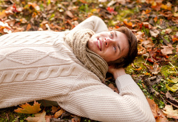 close up of smiling young man lying in autumn park