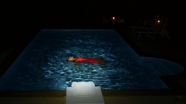Young Girl Swims in the Pool at Night. Slow Motion.