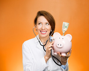 Doctor, nurse listening with stethoscope to piggy bank