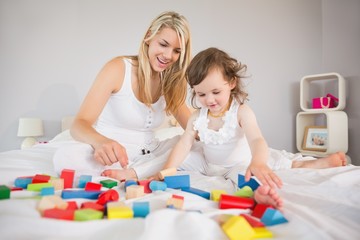Mother and daughter playing with building blocks on bed