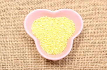 Millet groats in pink bowl on jute canvas