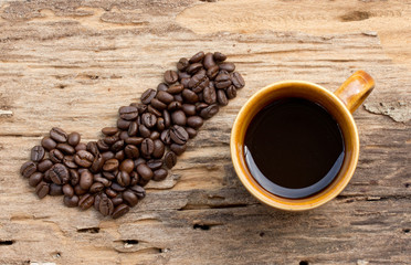 Checkmark from coffee beans and cup of coffee on wood background
