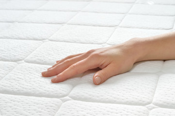 Choosing mattress and bed. Close-up of female hand touching and testing mattress in a store. Copy space.